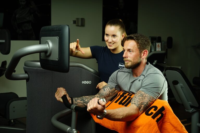Eine Trainerin erklärt einem Mann im Fitnessstudio die Einstellungen an einem EGYM-Trainingsgerät.